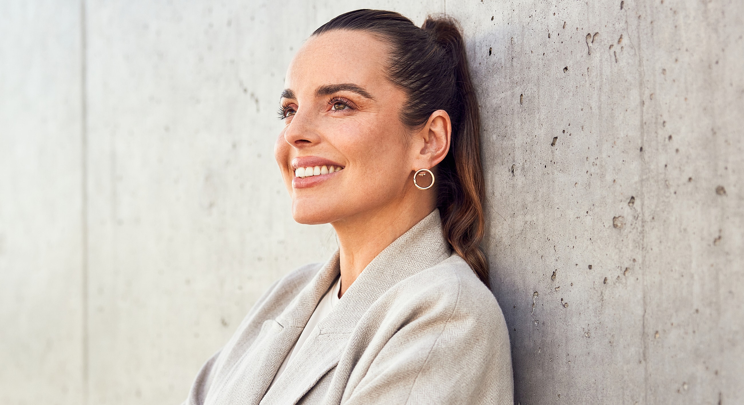 Smiling woman leaning against concrete wall.